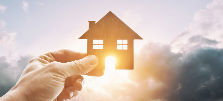 Hand holding cutout of a house in front of the sun