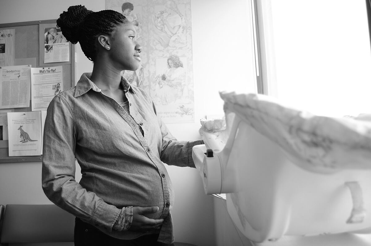 Pregnant mother looking out a window with baby seat