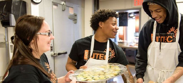 2 young men and 1 woman smiling while working in a kitchen