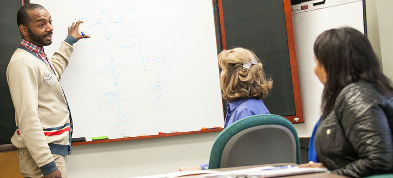 Man teaching at white board in front of 2 women