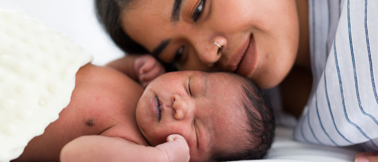 Woman lying her head next to a sleeping baby